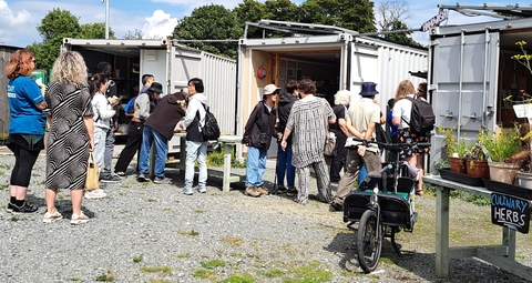A group of people outside, standing up, by some shipping containers