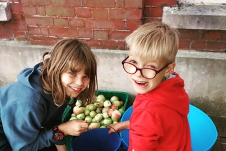 Two happy children looking at camera with a bucket of apples