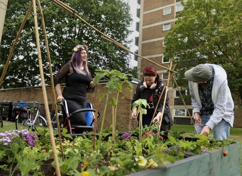 Three people around a raised planter of flowers and vegetables